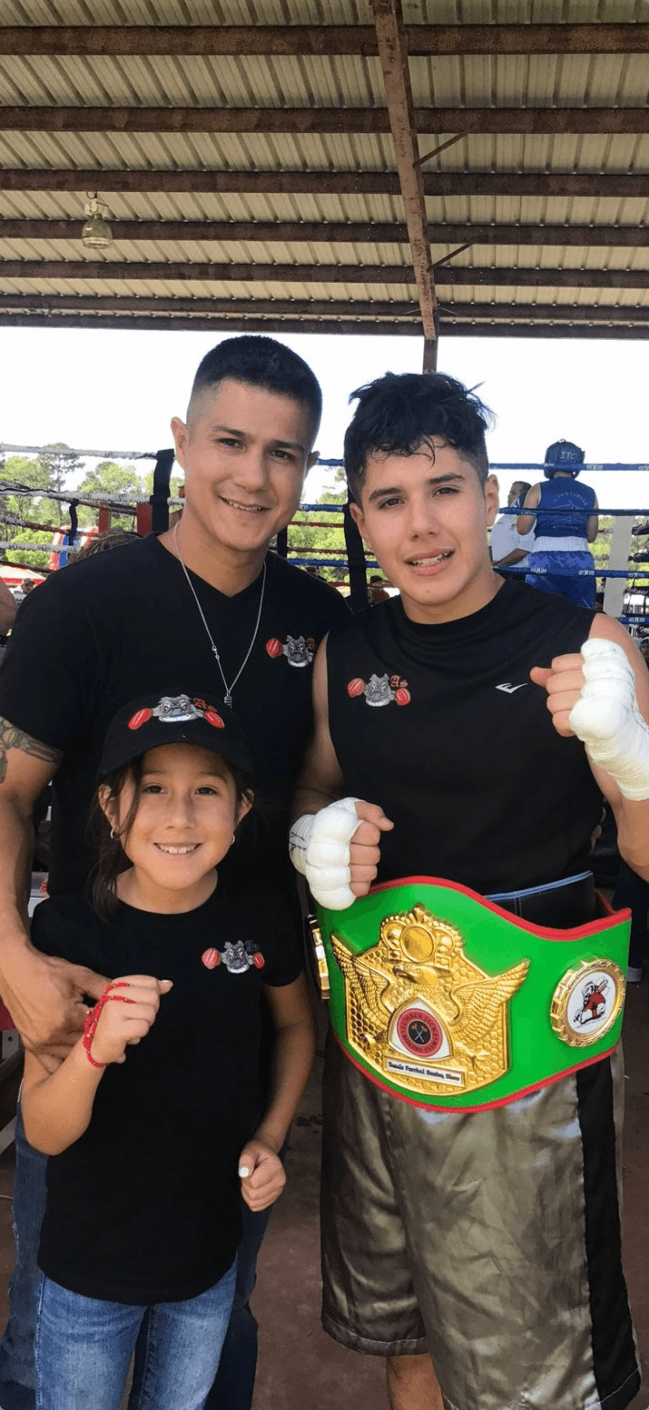A coach, a young fighter, and a parent at an outdoor boxing show